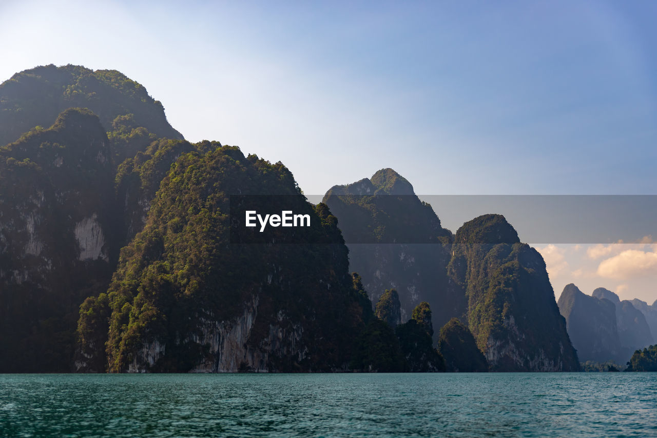 SCENIC VIEW OF ROCKS IN SEA BY MOUNTAINS AGAINST SKY