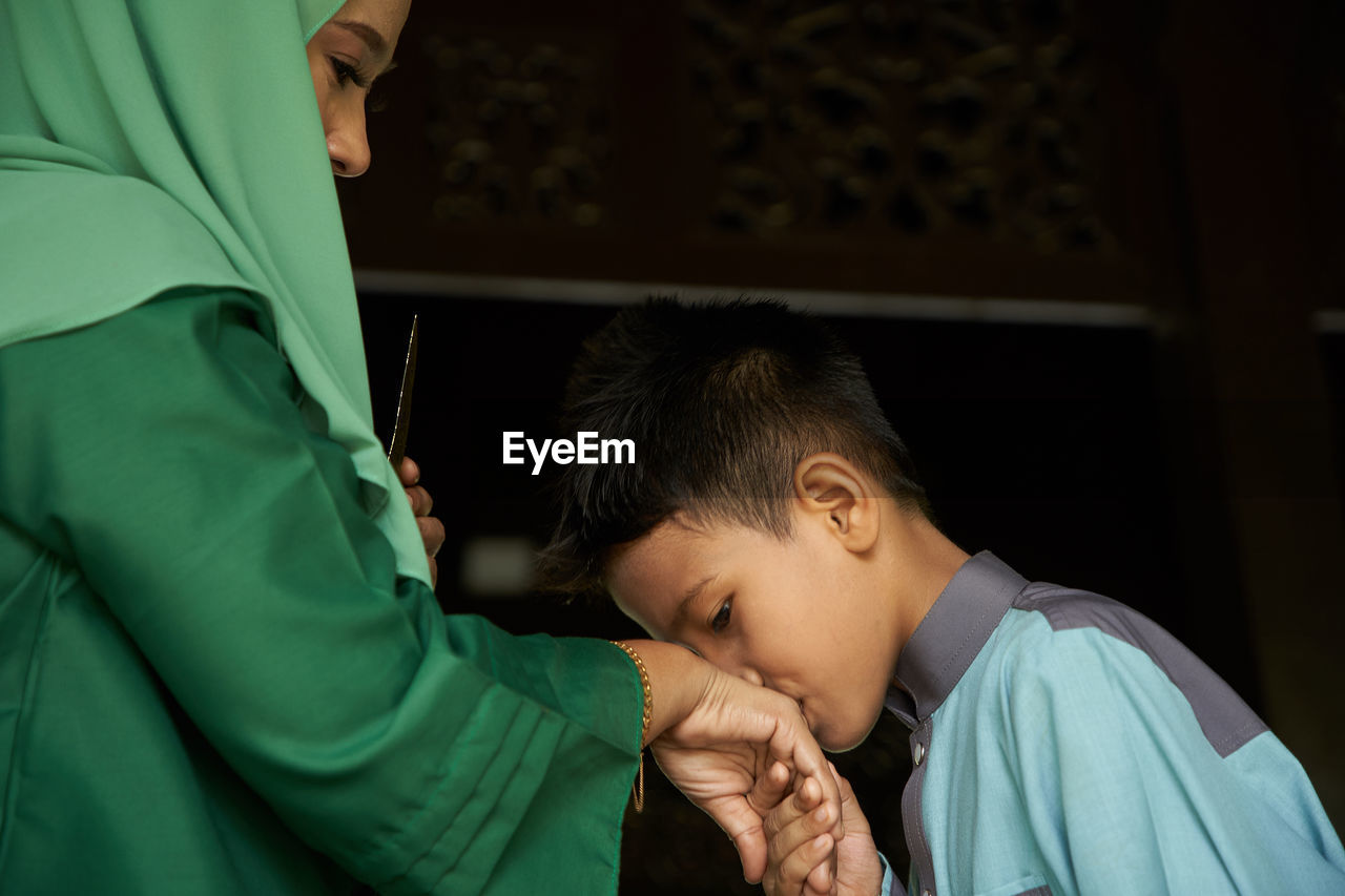 Profile view of malay son greeting and asking forgiveness to mother during ramadan festival 