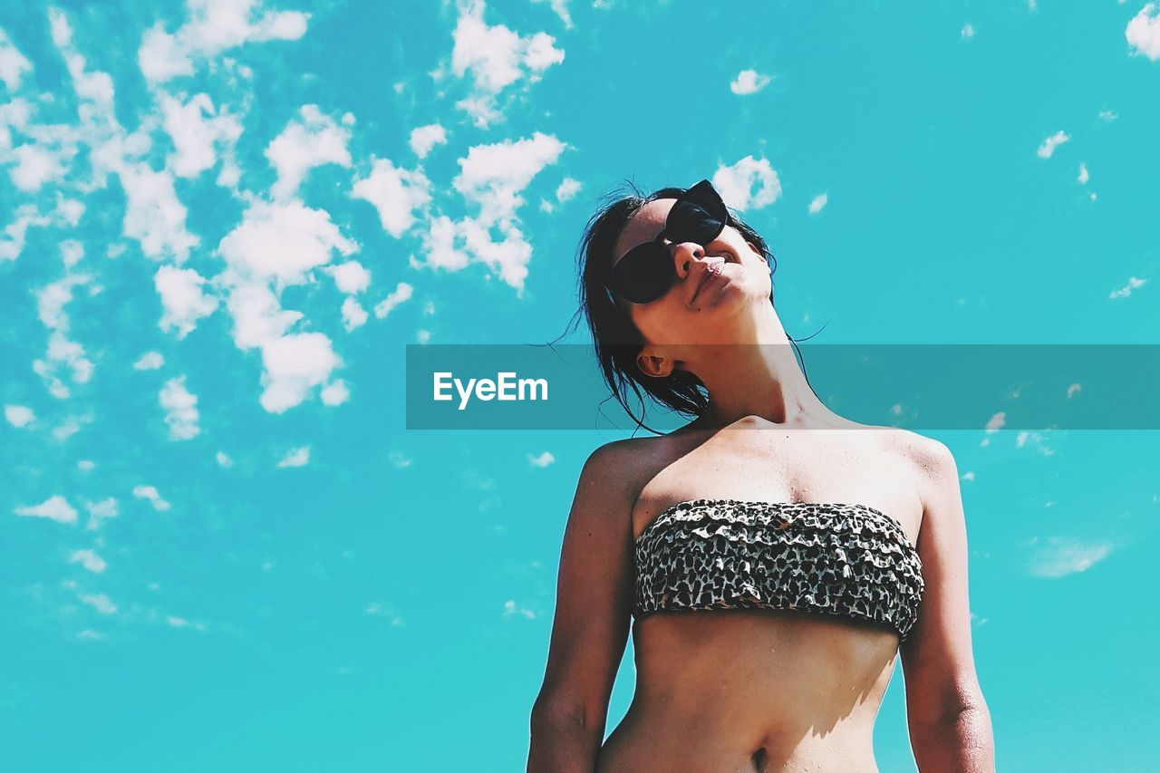 Low angle view of woman wearing sunglasses and bikini top against sky during sunny day
