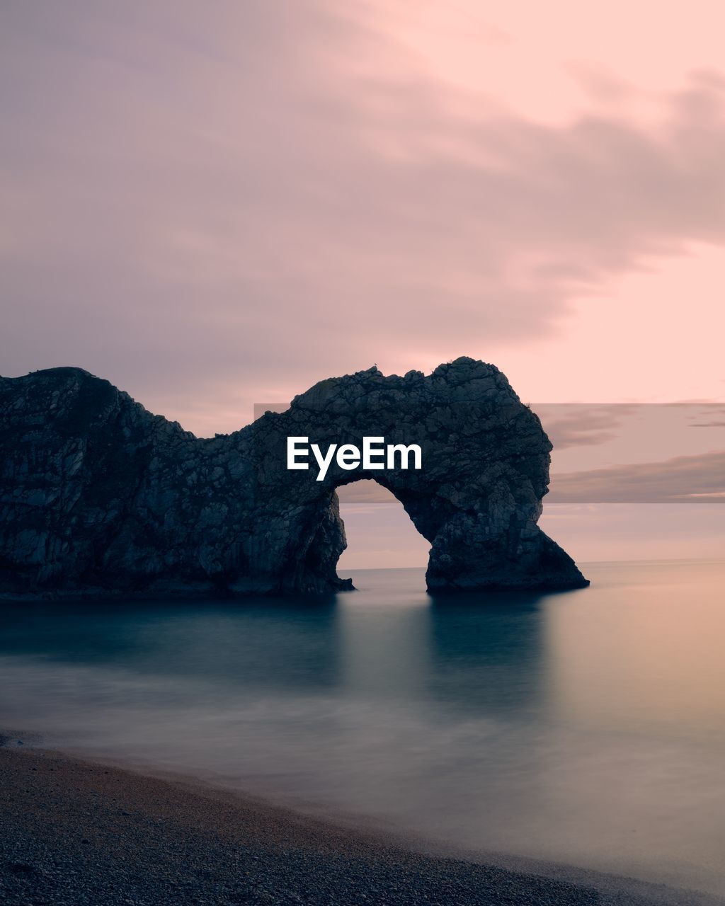 Rock formation in sea against sky during sunset