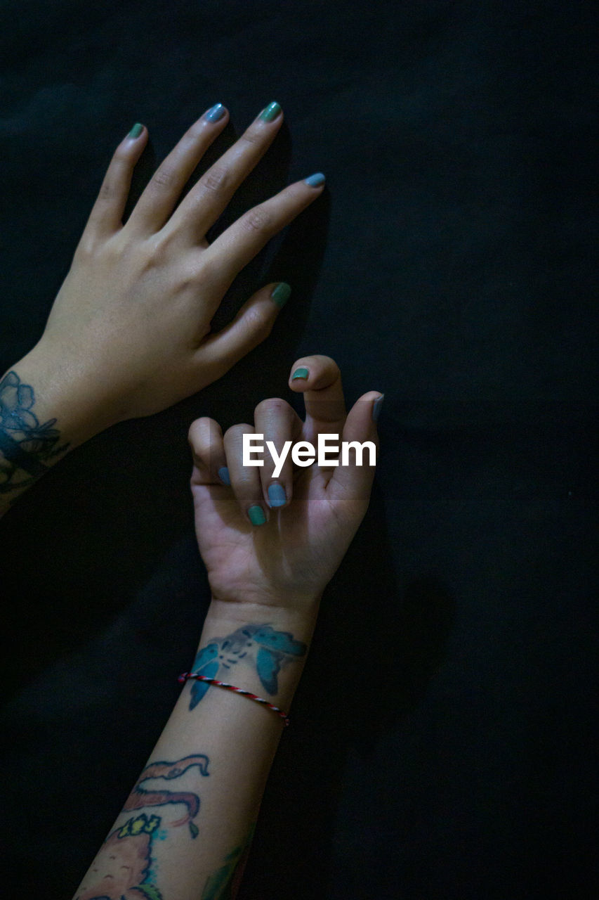 Cropped hands of woman with blue nail polish and tattoo over black background