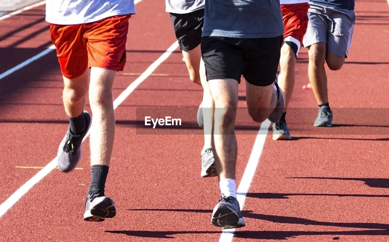 Close up of a group of high school boys running on a red track during track practice.