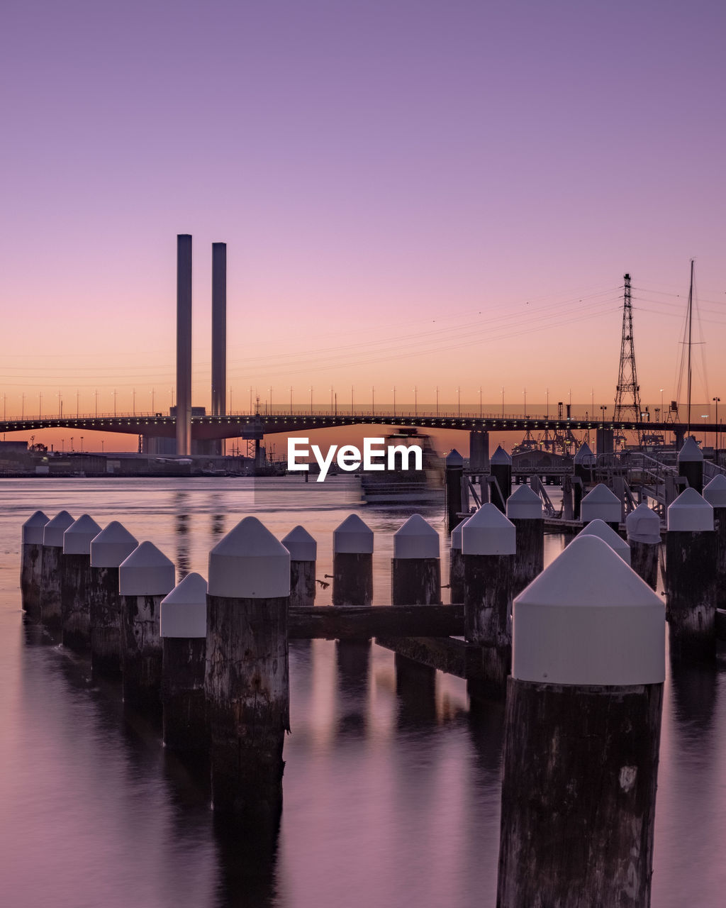 Bridge over river by buildings against sky at sunset