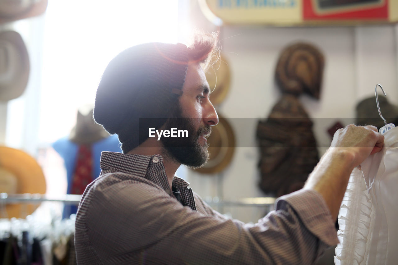 Side view of bearded man holding coathanger in clothing store