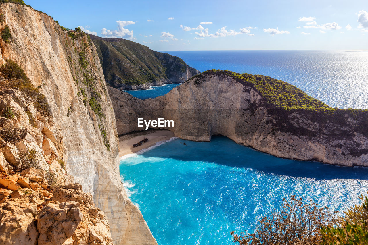 SCENIC VIEW OF SEA BY ROCKY MOUNTAINS AGAINST SKY