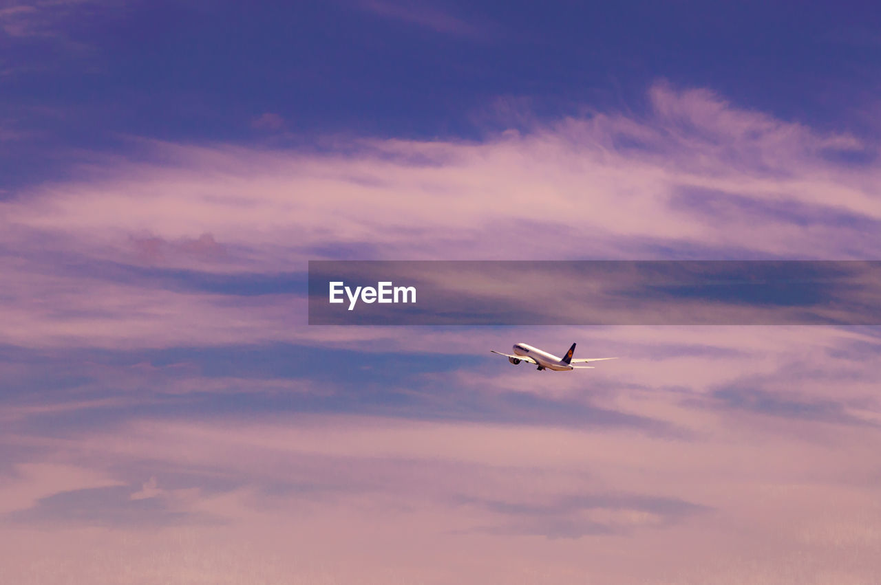 Low angle view of airplane flying against cloudy sky during sunset