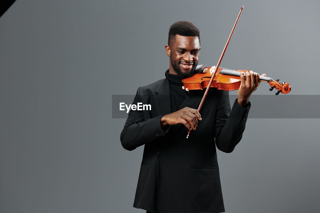 midsection of man playing violin against gray background