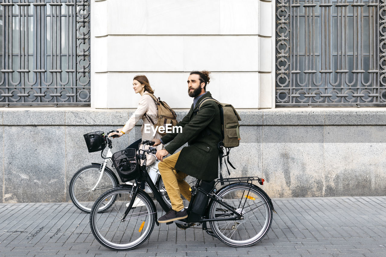 Couple riding e-bikes in the city passing a building