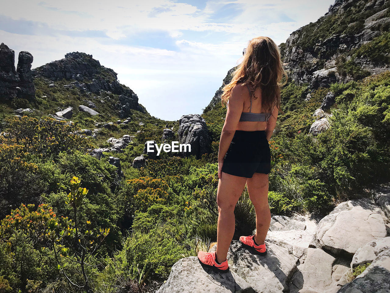 REAR VIEW OF YOUNG WOMAN STANDING ON ROCK