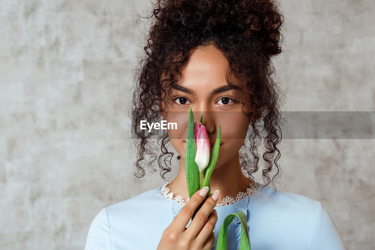 Portrait of smiling young woman holding tulip while standing against wall