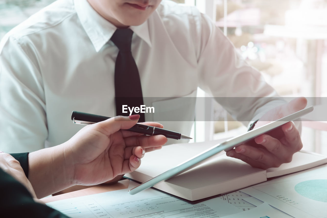 Midsection of businessman holding digital tablet while discussing with female colleague at desk in office