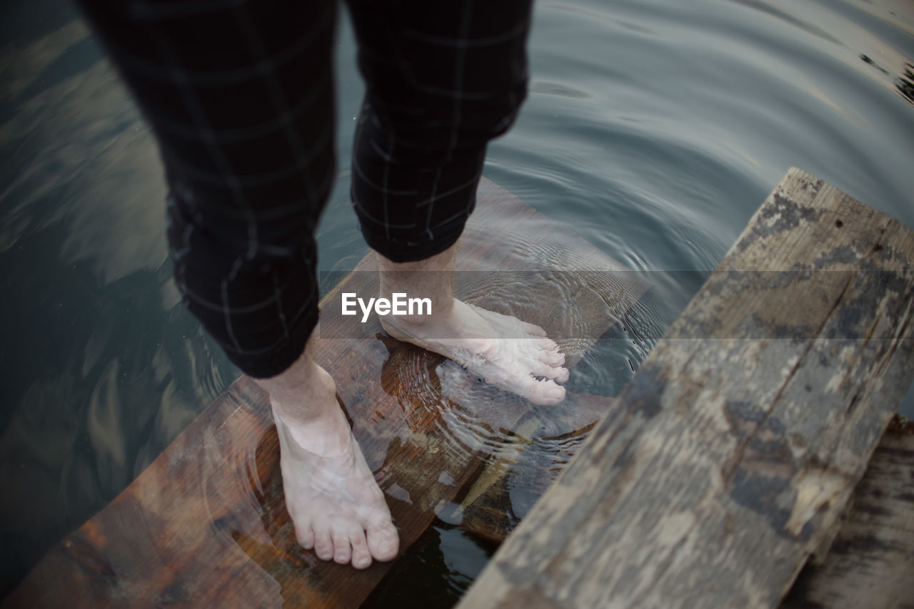 Low section of woman standing on wood by lake