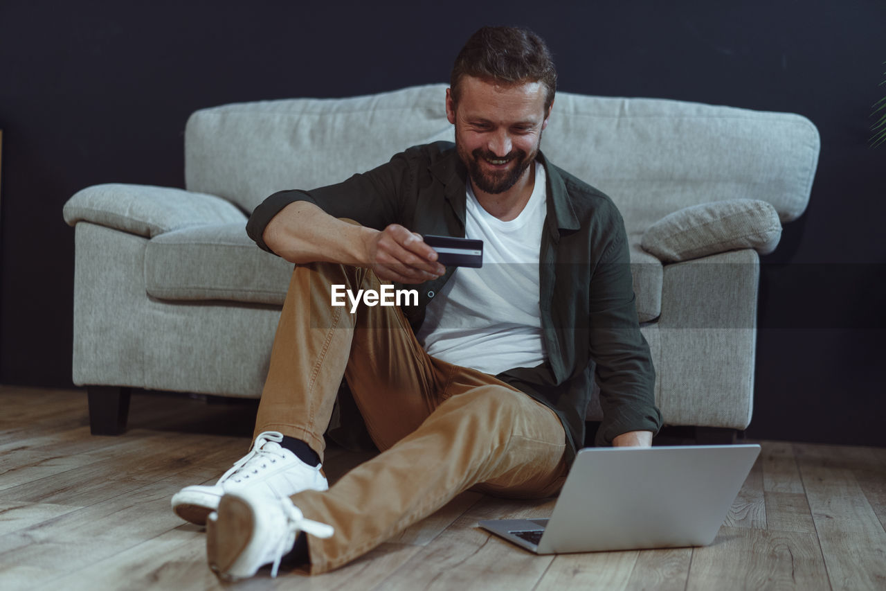 portrait of man using laptop while sitting on sofa