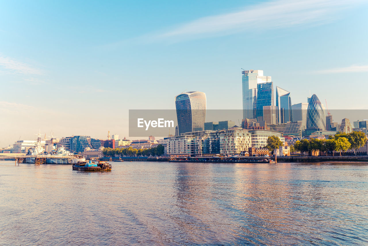 City by river and buildings against sky
