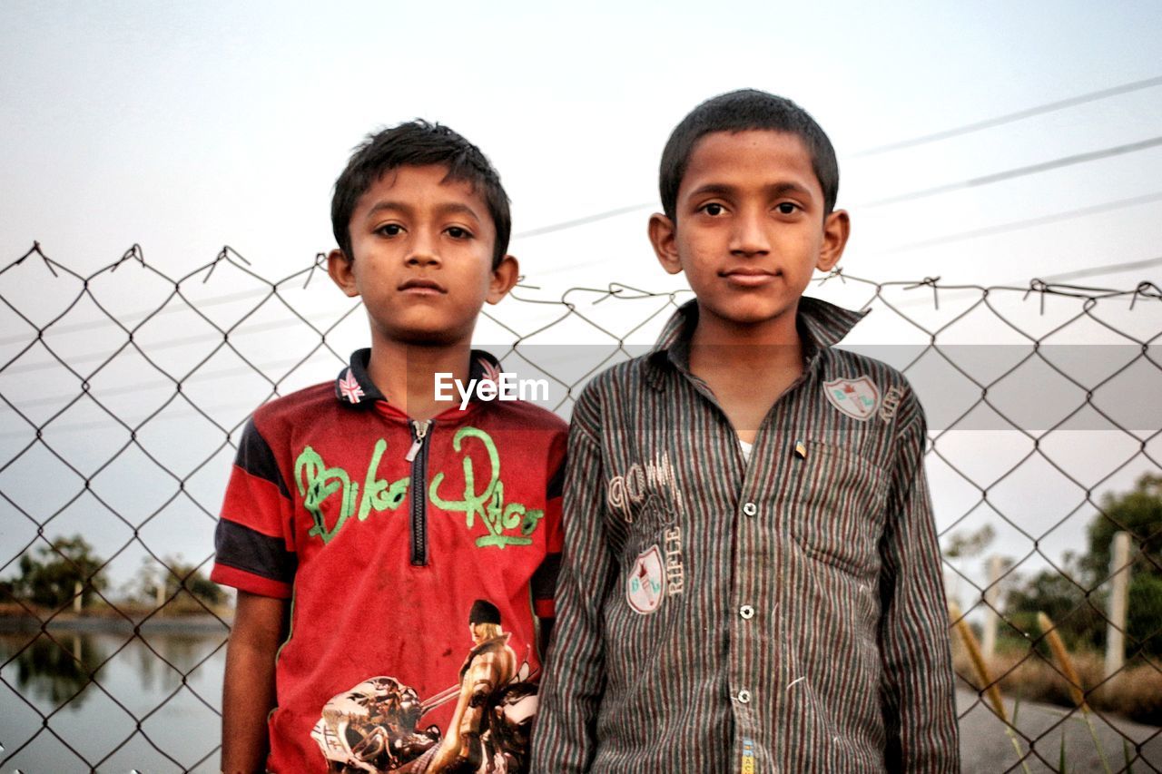 Portrait of boys standing against chainlink fence