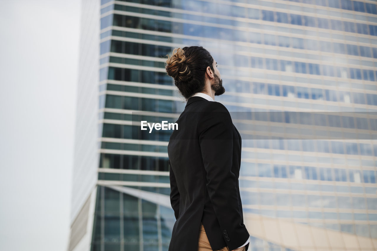 Businessman with hands in pockets looking away while standing against building