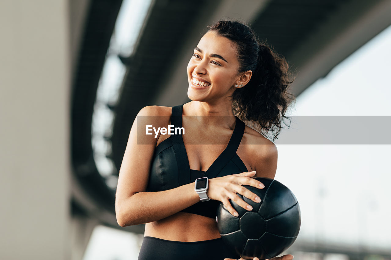 YOUNG WOMAN SMILING WHILE STANDING AGAINST WALL