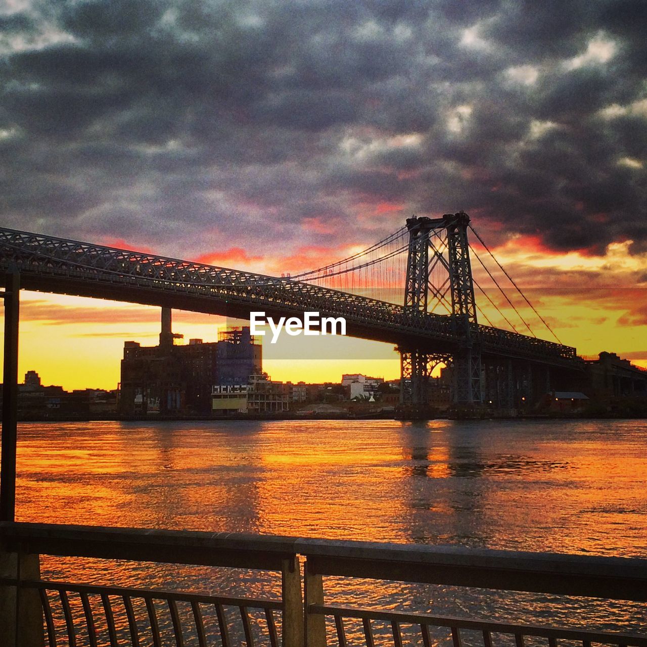 SUSPENSION BRIDGE OVER RIVER AGAINST CLOUDY SKY