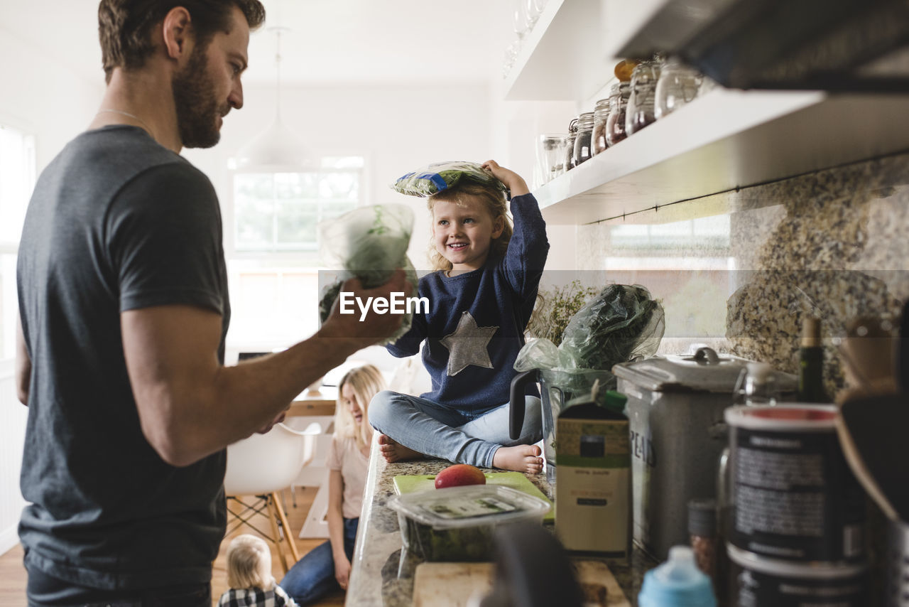 Smiling daughter looking at father while sitting on kitchen counter at home