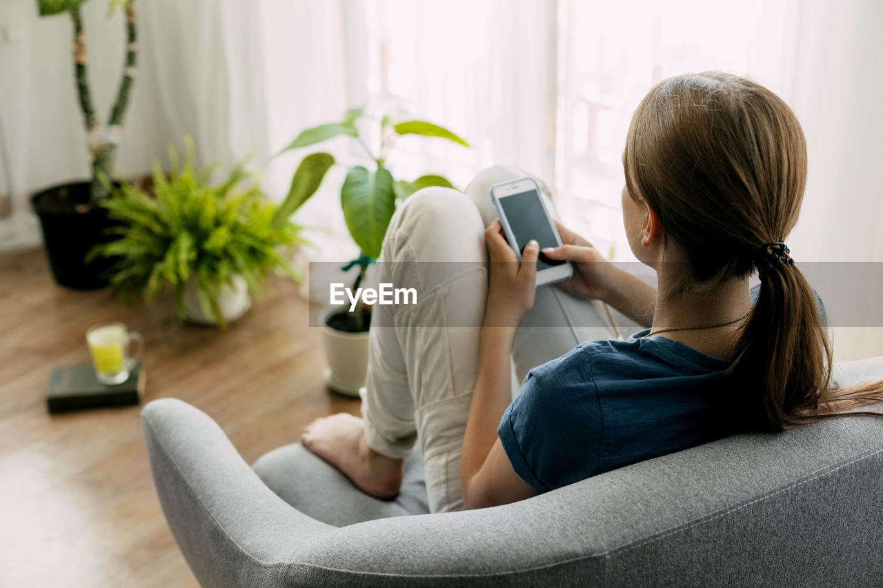 A young girl is sitting in a chair and exchanging messages online on her phone. home recreation