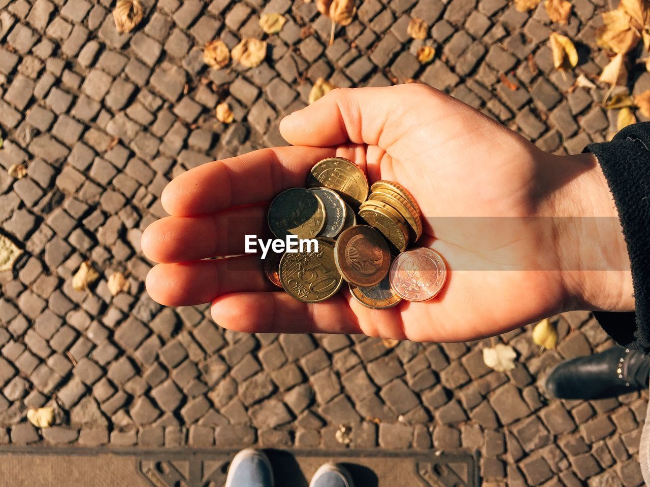 Low section of person with coins standing on street during sunny day