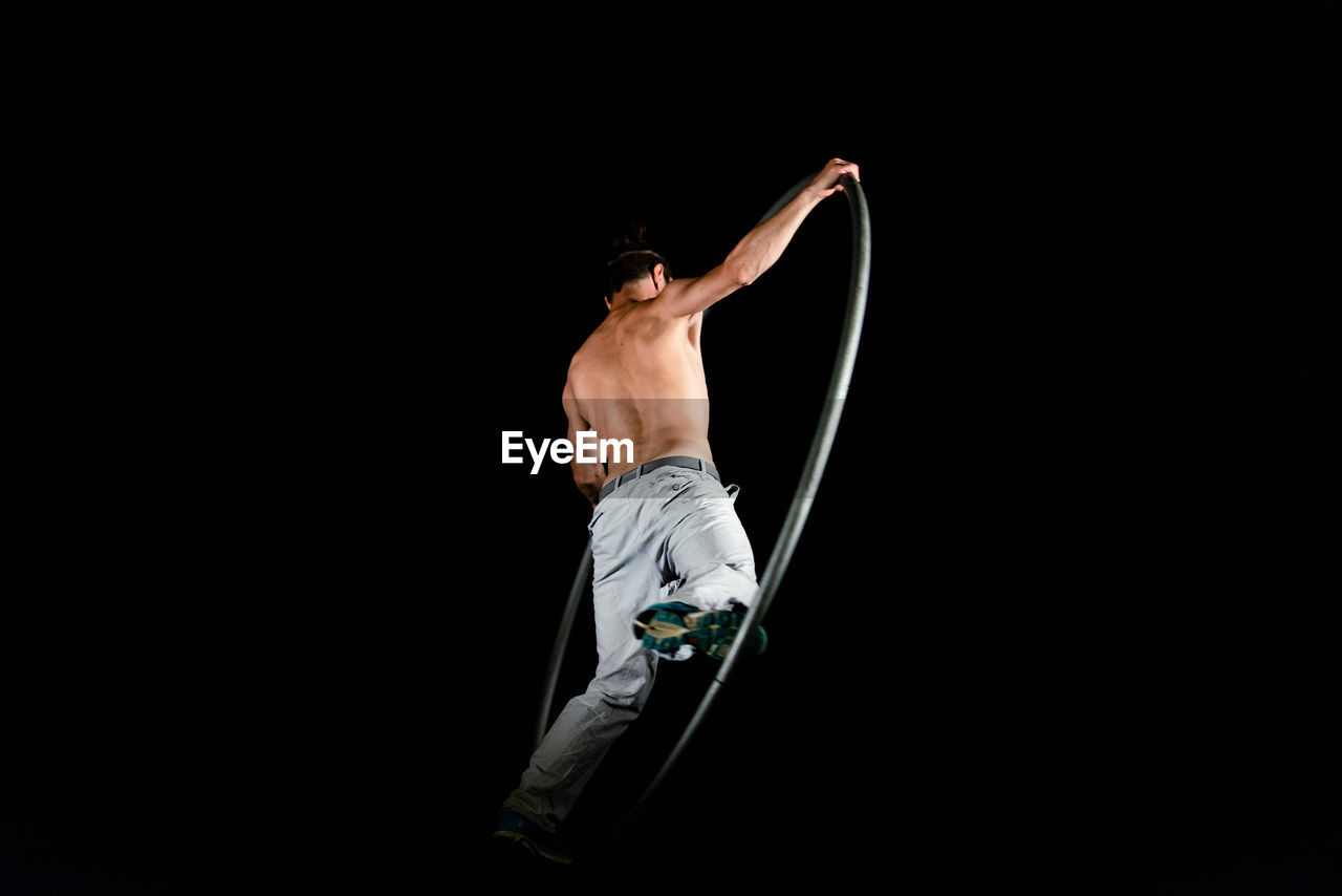 MIDSECTION OF SHIRTLESS MAN HOLDING PAPER AGAINST BLACK BACKGROUND