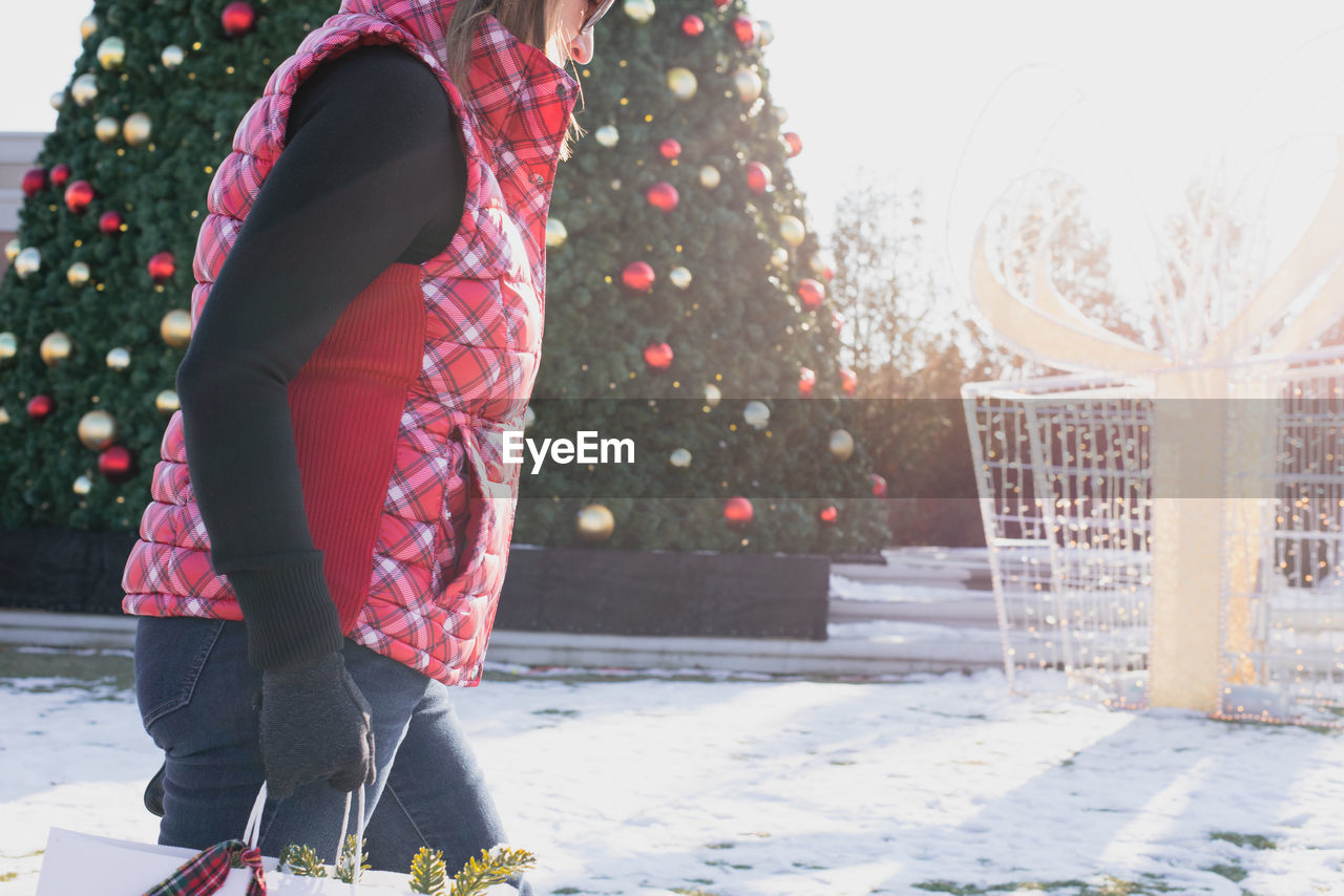 Midsection of woman standing against christmas tree during winter