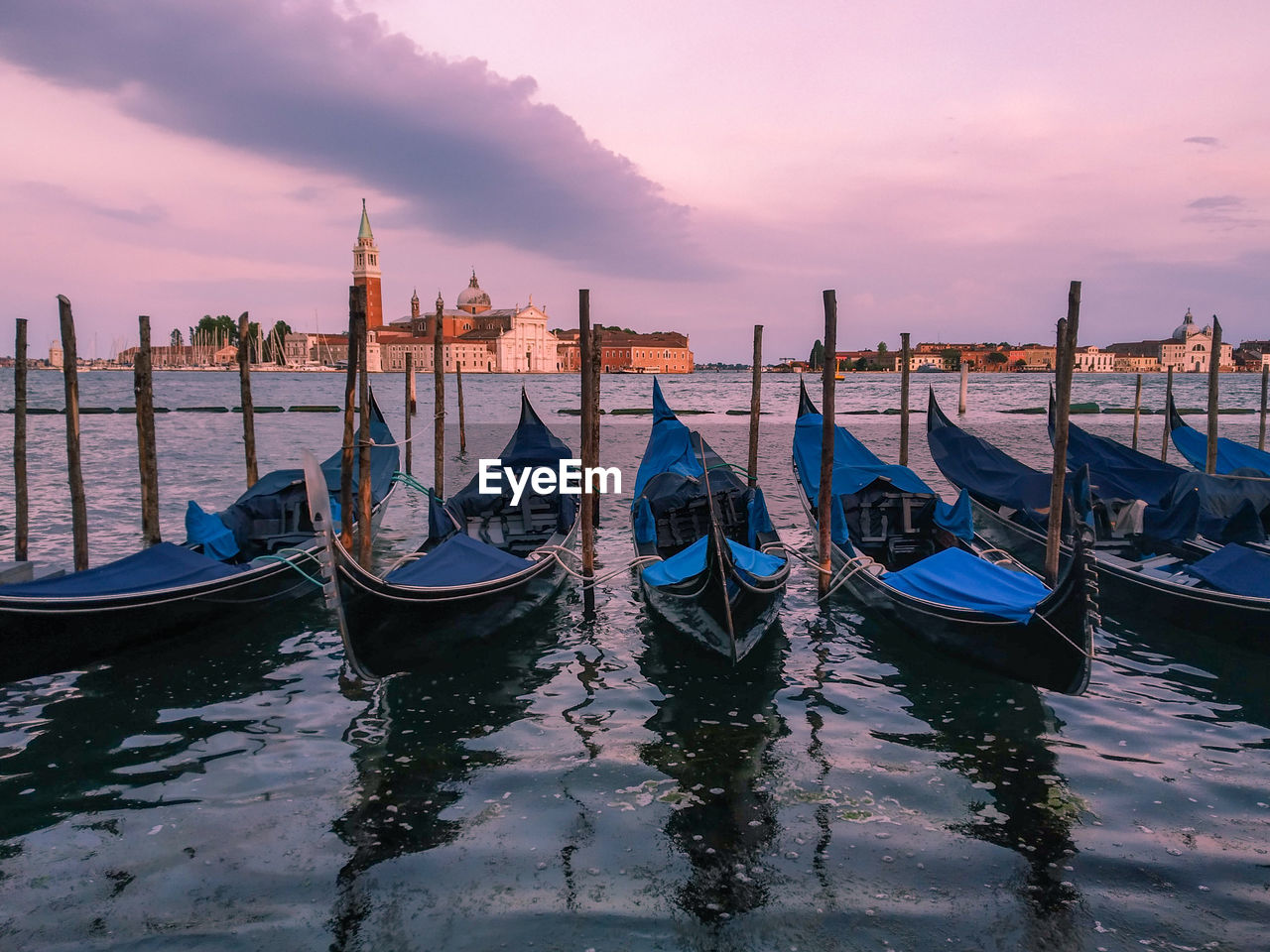 Boats moored in canal at sunset