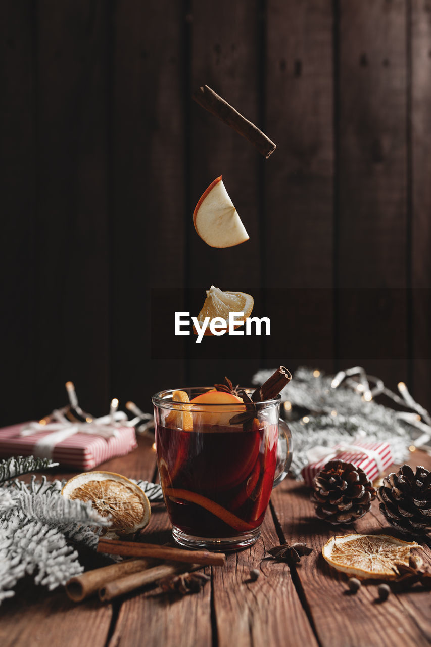 Christmas cup of mulled wine on table, levitating cinnamon stick, orange, apple