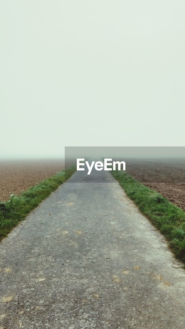 EMPTY ROAD AMIDST FIELD AGAINST CLEAR SKY