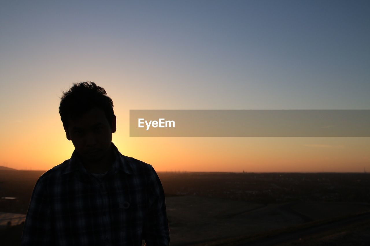 Young man standing against landscape during sunset