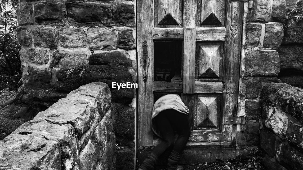 REAR VIEW OF MAN STANDING BY OLD BUILDING