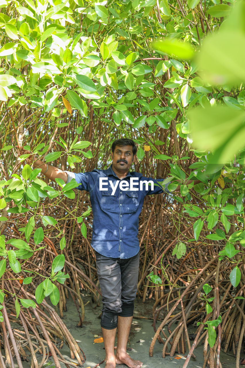 one person, plant, full length, front view, standing, growth, casual clothing, leisure activity, men, nature, tree, jungle, agriculture, land, day, lifestyles, looking at camera, portrait, outdoors, green, forest, leaf, young adult, plant part, childhood, smiling, child, rainforest, adult, crop, natural environment, plantation, flower, beauty in nature, happiness