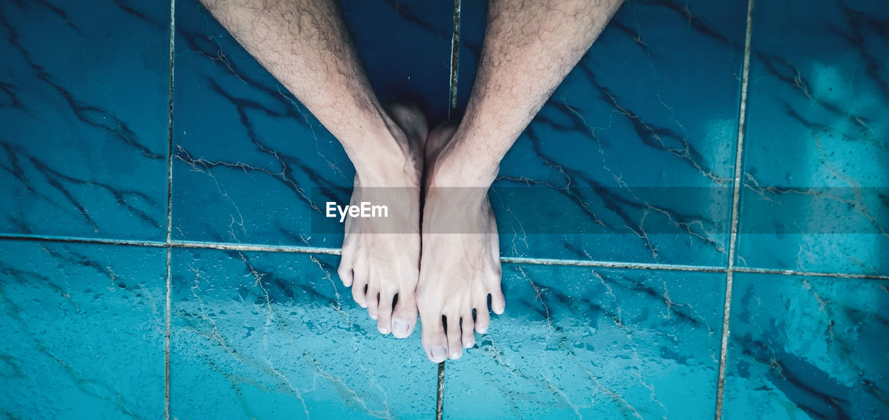 Low section of person standing by swimming pool