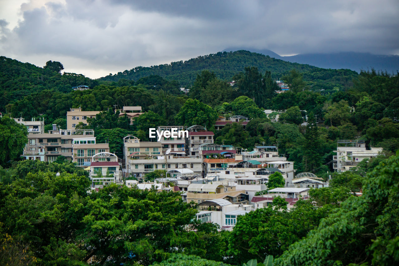 Buildings amidst trees and mountains against cloudy sky
