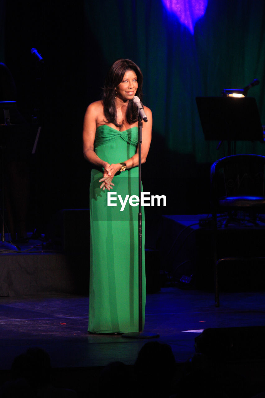 FULL LENGTH OF A WOMAN STANDING IN ILLUMINATED STAGE