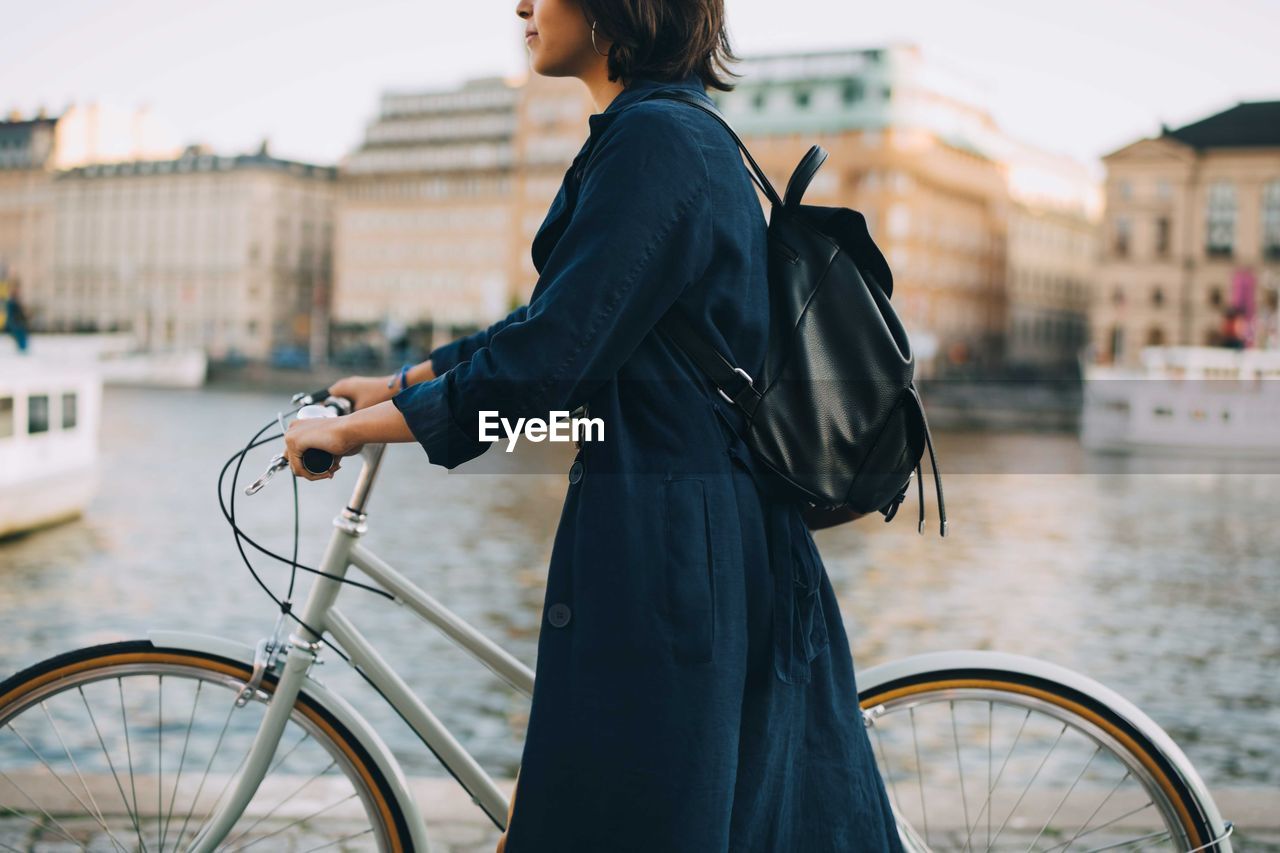 Midsection of young woman with bicycle crossing river in city