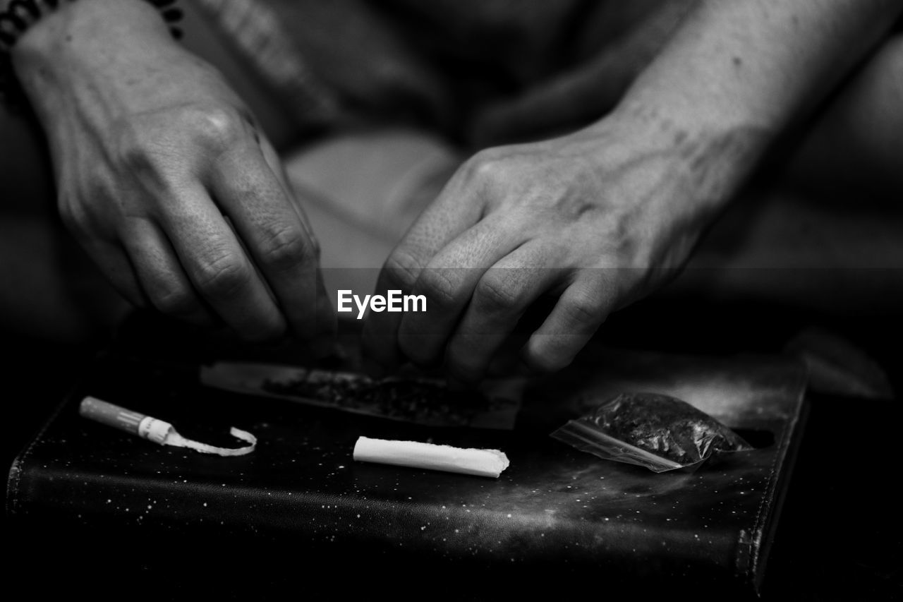 Cropped image of woman rolling marijuana joint on table