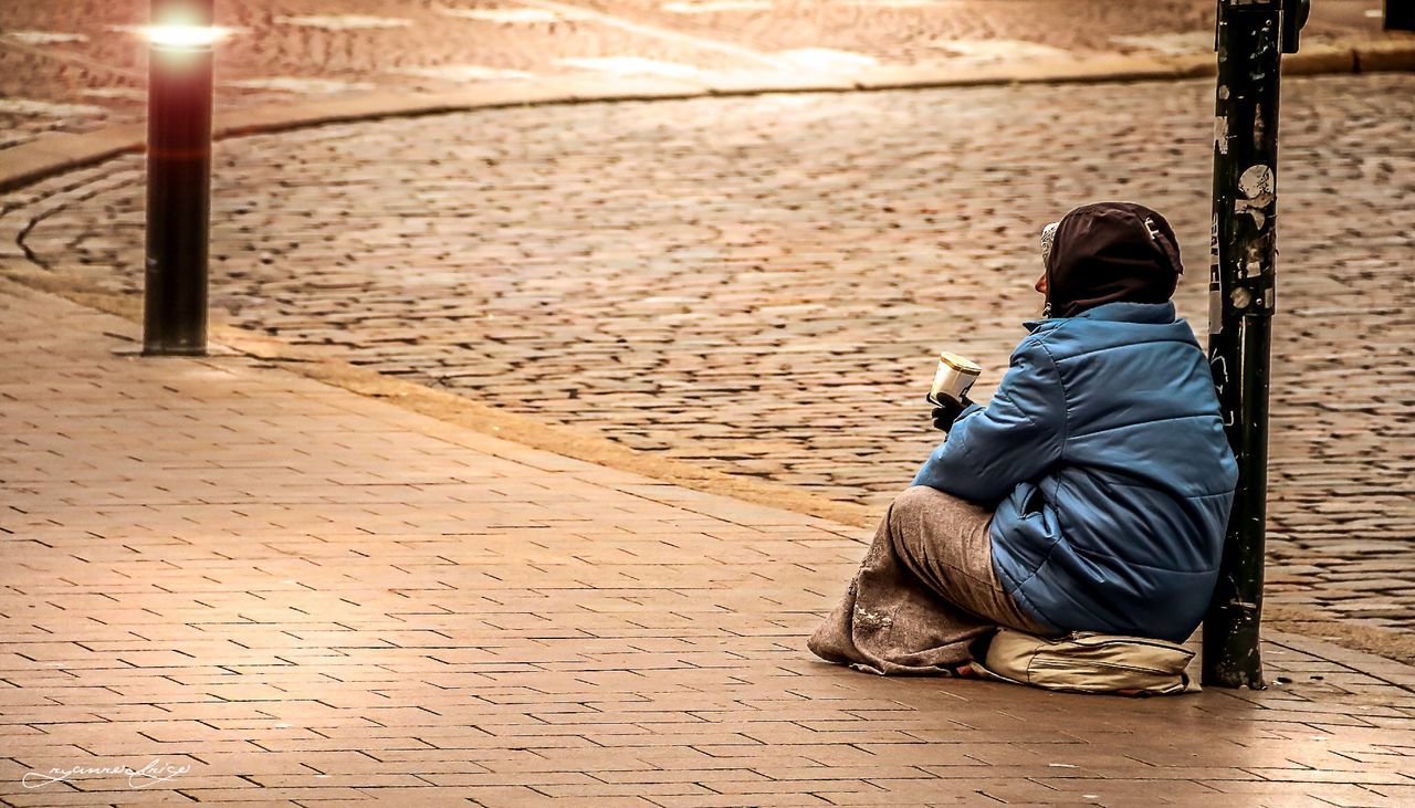 Full length rear view of woman begging on sidewalk