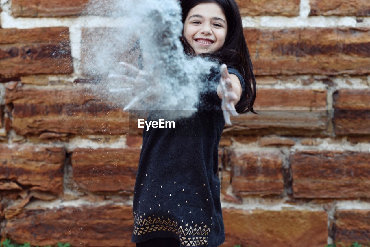 Playful girl playing with glitter against brick wall