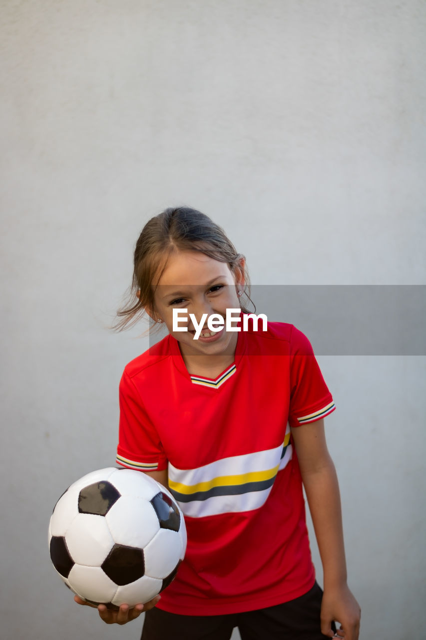 Portrait of smiling girl holding soccer ball against white background