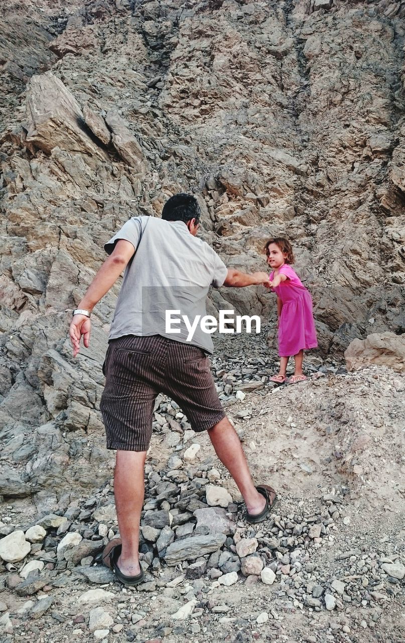 Rear view of father pulling daughter while standing on rocks