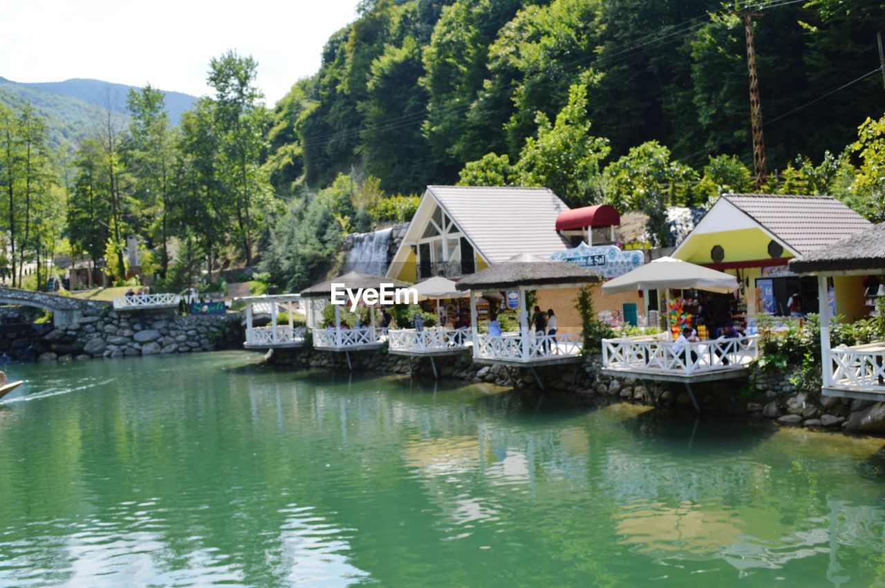 HOUSES BY RIVER AGAINST TREES AND BUILDINGS