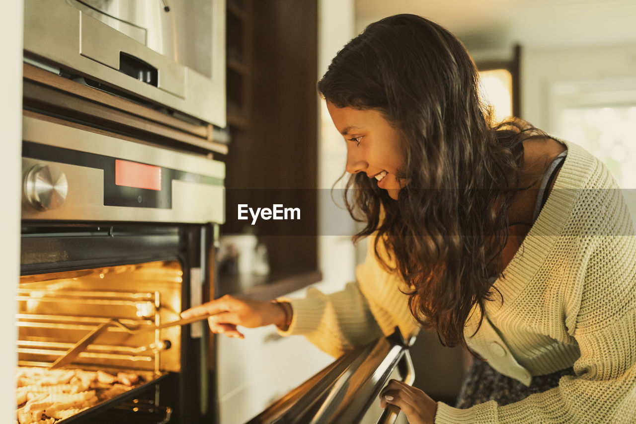 Smiling girl checking food while opening oven door