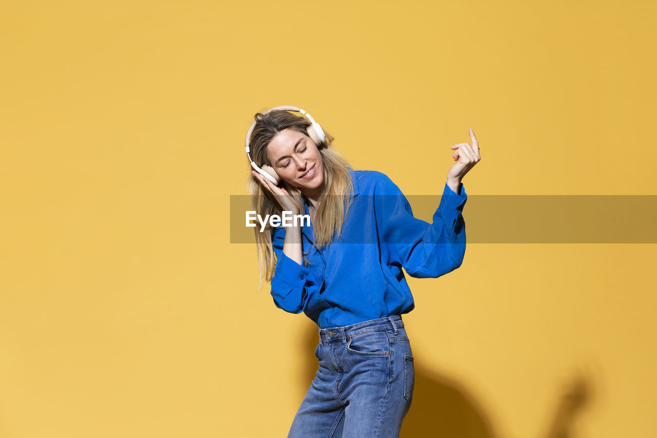 Woman listening music and dancing against yellow background