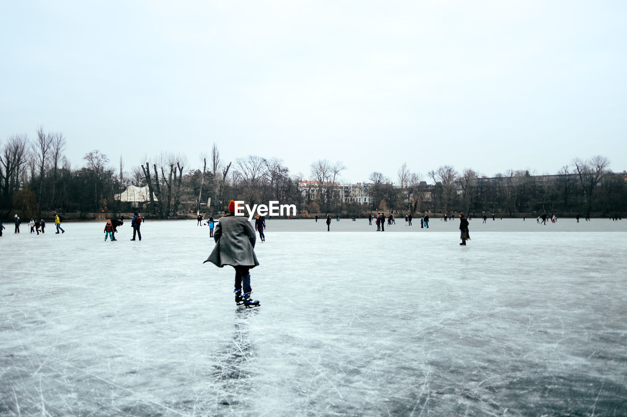 People on frozen lake against sky during winter