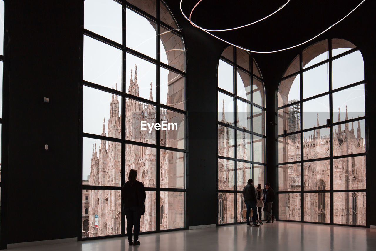 People standing by glass windows with milan cathedral in background