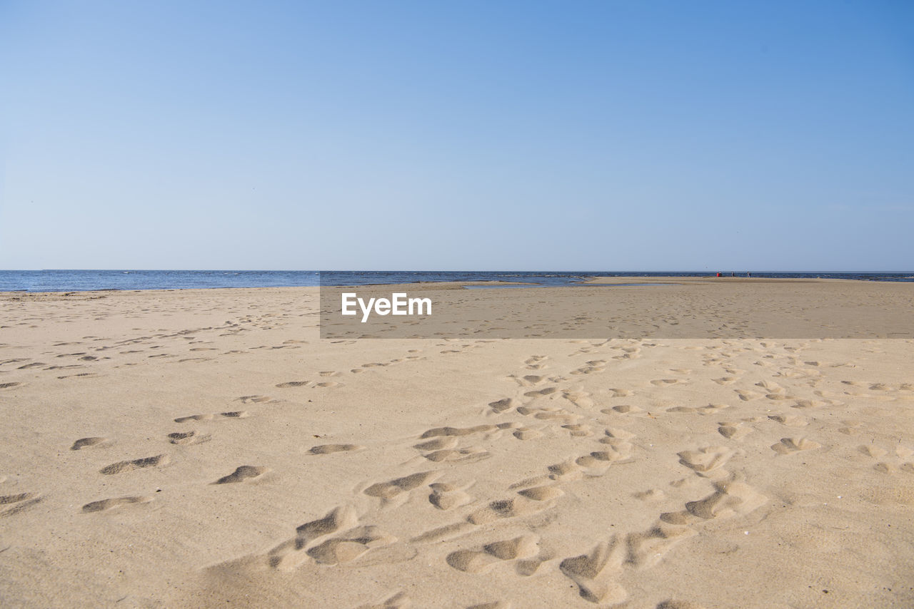 FOOTPRINTS ON BEACH AGAINST CLEAR SKY