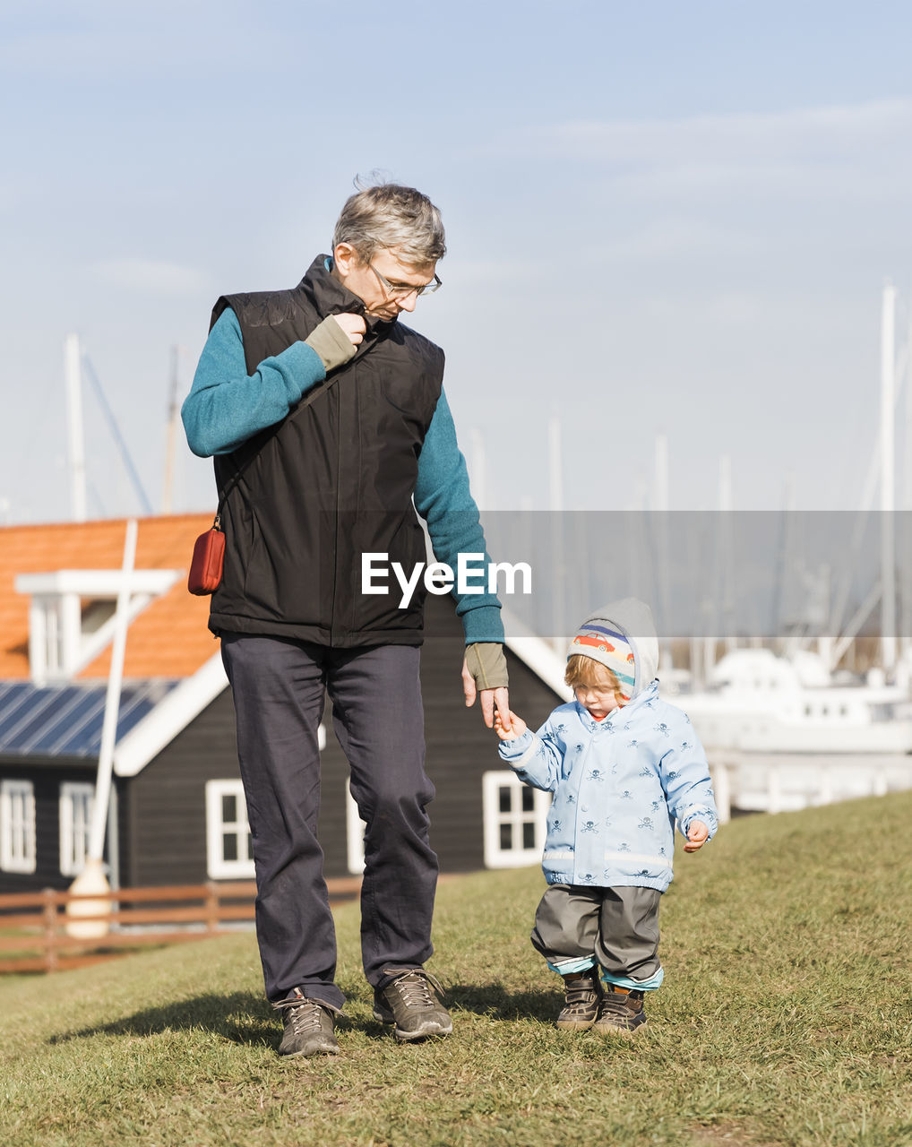 Grandfather and granddaughter walking on field against sky