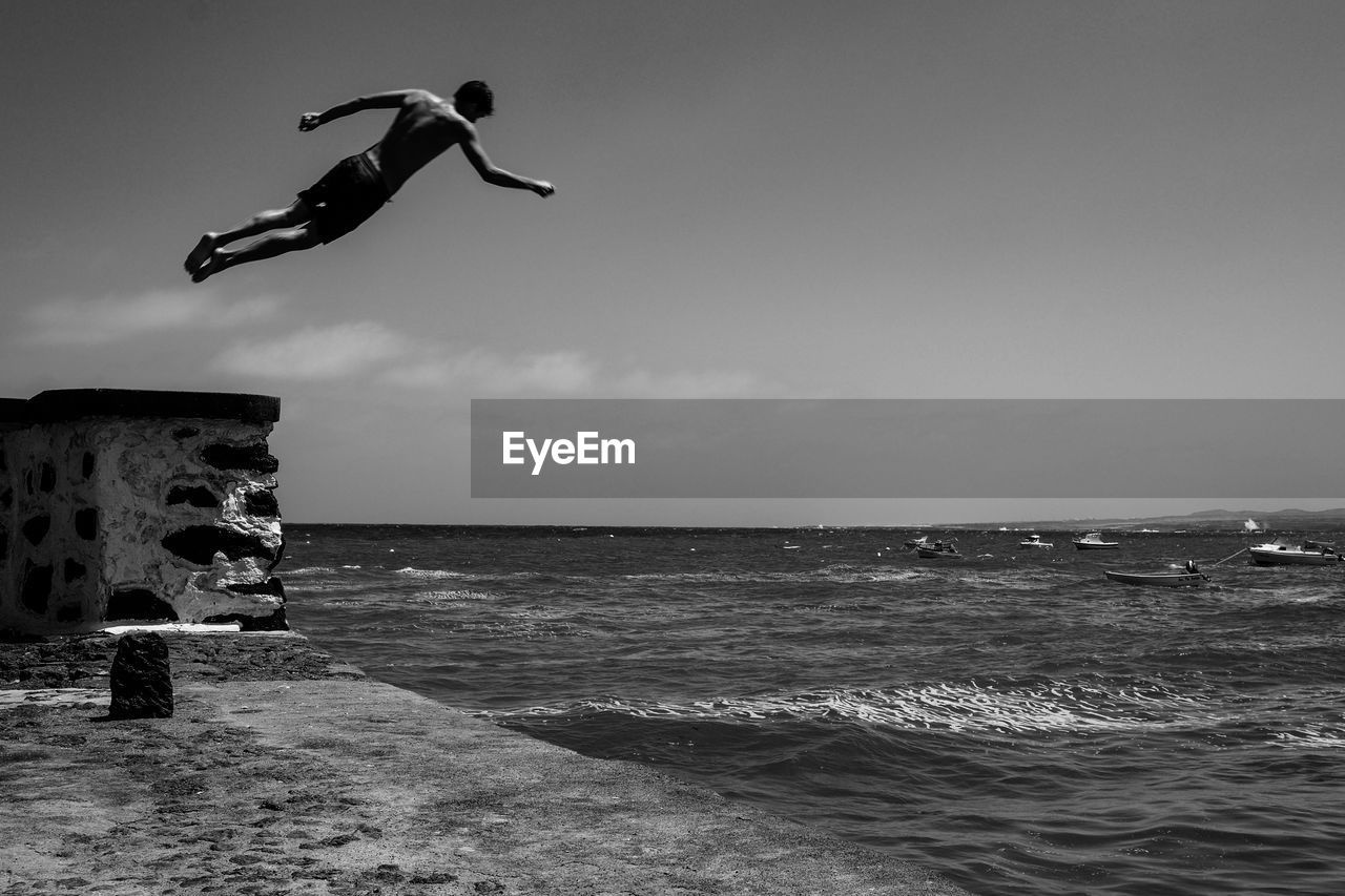 MAN JUMPING AT SEA AGAINST SKY